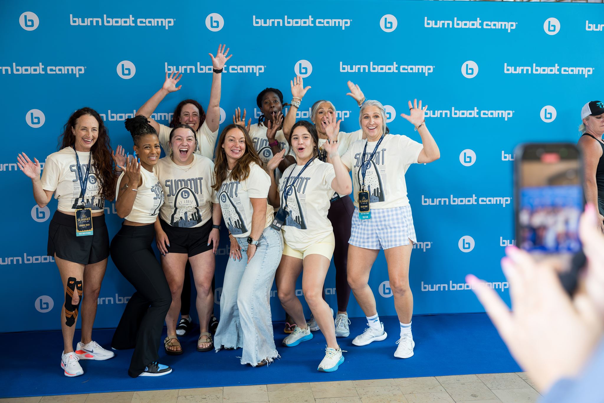 Burn Boot Camp Summit attendees smiling and waving in front of a Burn Boot Camp backdrop
