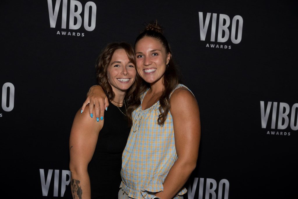 Alayna Tichenor and Carmen Hansen smile together in front of the VIBO Awards backdrop