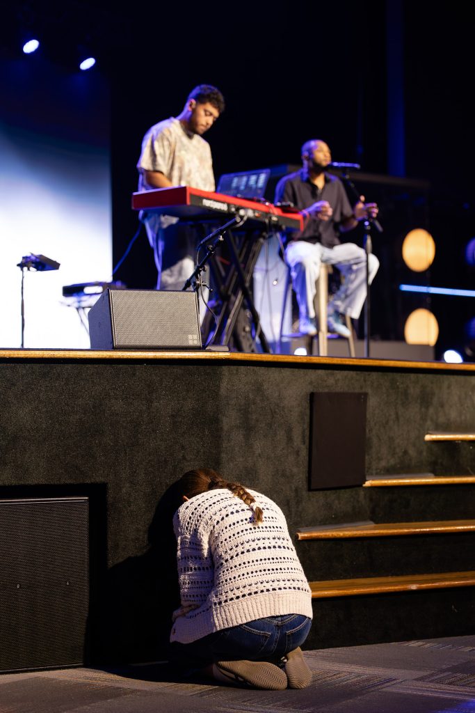 An attendee kneels in prayer near the stage during a Roundup worship session.